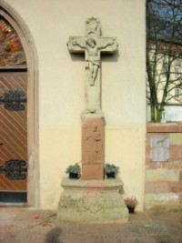 Une croix du XVIIIe siècle est adossée à la façade de la chapelle de l'Étang à Bitche, figurant saint Nicolas sur le fût.