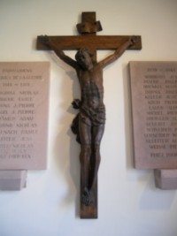 Un crucifix en bois est encadré par les deux plaques en grès du monument aux morts de la paroisse, sous le porche de l'édifice.