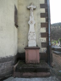 Adossée à la façade de l'église paroissiale de Roppeviller, une croix datant du XIXe siècle représente la Sainte Famille en marche sur le registre inférieur du fût-stèle. Un cœur rayonnant la surplombe, tandis que le socle d'origine a été remplacé.