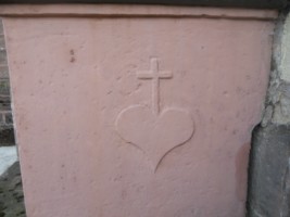 Un cœur crucifère est représenté de part et d'autre du socle de la croix, sur les faces droite et gauche.
