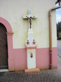 Une croix de chemin se situe en bordure de la rue de Sarreguemines, adossée à la façade de la petite chapelle de la Très Sainte-Trinité. Datant peut-être du XIXe siècle, elle figure Notre-Seigneur Jésus-Christ en Croix, la colombe du Saint-Esprit, deux coeurs enflammés dans une nuée, ainsi qu'un cœur enflammé dans une guirlande. Il s'agit d'une croix avec socle et fût-stèle droit, et croisillon en croix latine.