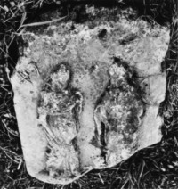 Deux personnages non identifiés sont représentés sur un fragment de l'ancienne croix, posé à terre (photographie du service régional de l'inventaire de Lorraine).
